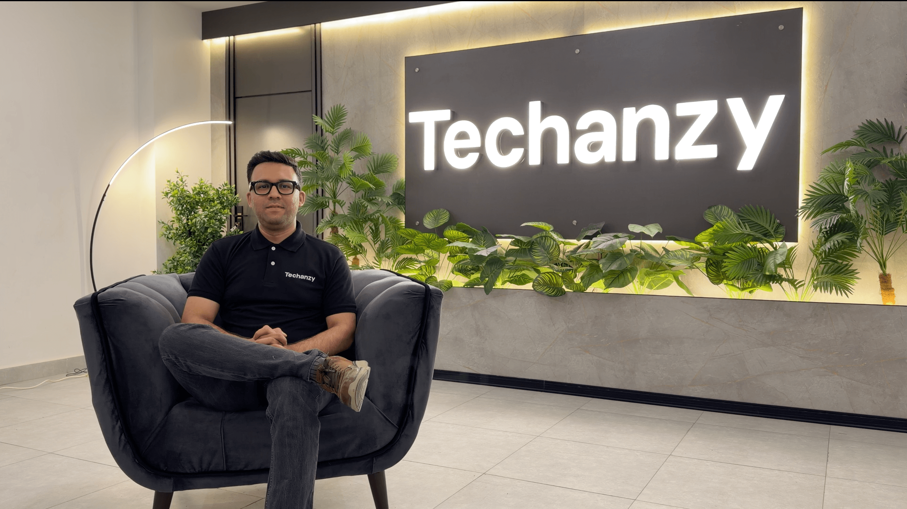 Muhammad Shahzeb seated in the Techanzy office, with the Techanzy logo on the wall behind him